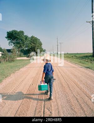 Etats-Unis, Minessota, vue arrière d'un jeune Amish marchant sur la route de terre et transportant le refroidisseur Banque D'Images