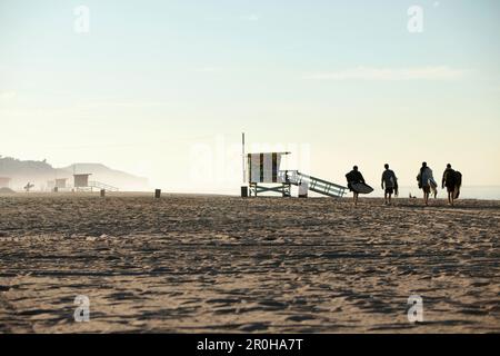 Etats-Unis, Californie, Malibu, les surfeurs marchent sur le sable vers l'eau à Zuma Beach Banque D'Images