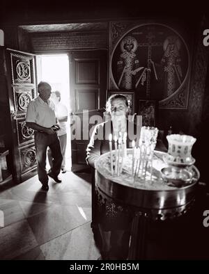 GRÈCE, Chora, île du Dodécanèse, une femme allume des bougies à l'intérieur de St. Cathédrale de John's au sommet de l'île dans le village de Chora (B&W) Banque D'Images