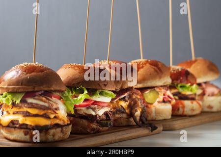 Beaucoup de hamburgers différents avec des ingrédients sur une assiette en bois Banque D'Images