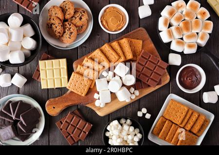 Table de buffet Smores. Guimauves grillées, craquelins, chocolat et assortiment d'ingrédients. Vue de haut en bas sur un arrière-plan en bois sombre. Banque D'Images