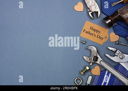 Étiquette cadeau Happy Pères Day avec bordure latérale de liens et d'outils sur fond de papier gris bleu. Vue de dessus avec espace de copie. Banque D'Images