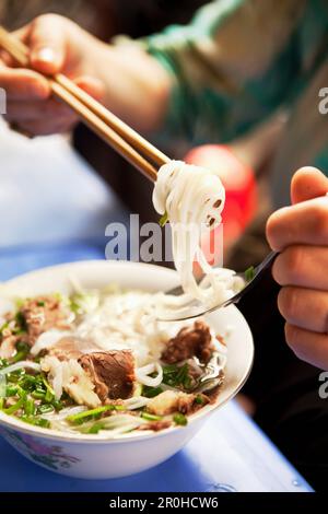 VIETNAM, Hanoi, restaurant Pho Gia Truyen, également connu sous le nom de 49 Bat Dan, une femme mange une bouchée de pho bo (bol de nouilles de boeuf) de la manière traditionnelle avec un sp Banque D'Images