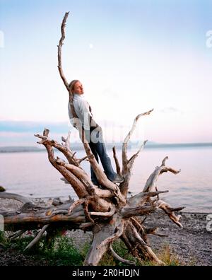 USA, Wyoming, jeune femme debout sur un arbre mort avec les mains dans les poches, lac Yellwostone, parc national de Yellowstone Banque D'Images