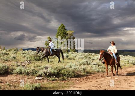 USA, Wyoming, du cantonnement, un homme et une femme monter à cheval sous un ciel dramatique, Abara Ranch Banque D'Images