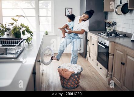 Les compétences d'une maman qui travaille. une jeune mère utilisant un téléphone portable tout en effectuant des travaux ménagers et en tenant son bébé à la maison. Banque D'Images