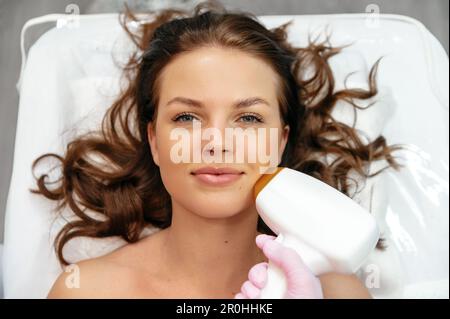 Épilation au laser sur le visage. Procédures du salon. Jeune femme caucasienne positive couché dans un salon de beauté pendant la procédure pour enlever les cheveux indésirables en utilisant l'enlèvement de cheveux au laser Banque D'Images
