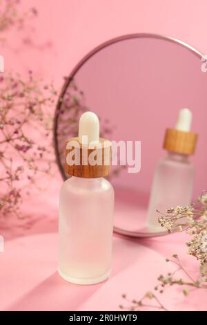 Bouteille de sérum pour le visage et belles fleurs près du miroir sur fond rose Banque D'Images