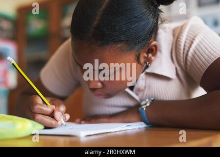 Cette somme mathématique nécessite toute mon attention. une jeune fille assise seule dans sa classe à l'école et écrivant dans son cahier d'exercices. Banque D'Images