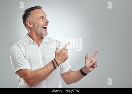 Wow, je ne peux pas croire cela. Photo studio d'un homme mature pointant vers l'espace de copie sur fond gris. Banque D'Images