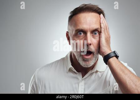 Oh non, j'ai complètement oublié. Portrait studio d'un homme mûr qui a l'air surpris sur fond gris. Banque D'Images