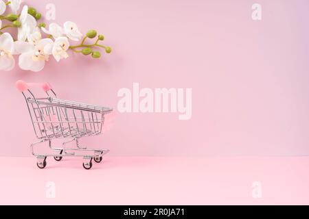 Vide jouet métal supermarché panier sur la couleur rose avec fleur blanche d'orchidée. Banque D'Images