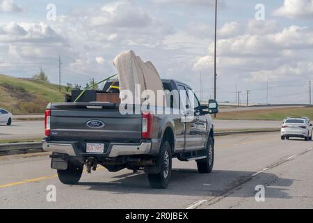 Calgary, Alberta, Canada. 7 mai 2023. Un pick-up chargé avec un vieux matelas à l'arrière, roulant sur une autoroute. Banque D'Images