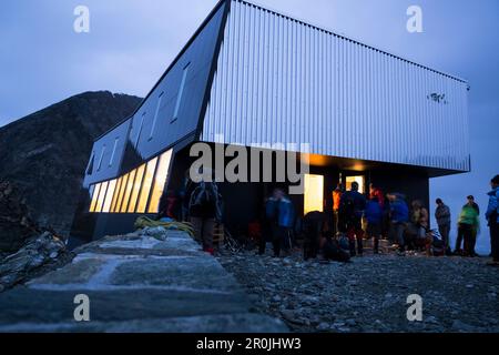 Tôt le matin, les alpinistes devant la nouvelle et moderne cabane de Tratuit se préparent à l'ascension du Bichorn, tandis que les fenêtres de la cabane sont sti Banque D'Images