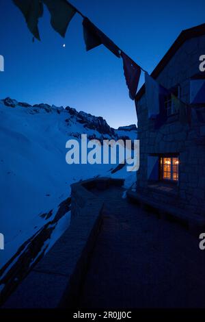 Lumière illuminant dans une fenêtre de la cabane Bachlial, tandis que la nuit tombe et la lune brille, vallée de Baechli, région de Grimsel, Alpes bernoises, canton de Banque D'Images