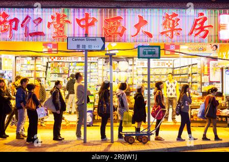 Les gens qui font la queue à un arrêt d'autobus, le soir, la pharmacie, la rue commerçante, les publicités, Scène de rue, zone commerçante Causeway Bay, Hong Kong, Chine, Asie Banque D'Images
