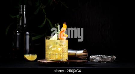 Cocktail alcoolisé à la pénicilline avec scotch, whisky, sirop de miel et de gingembre, jus de citron et glace en verre garni de zeste d'orange. Arrière-plan noir Banque D'Images