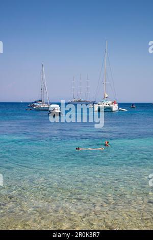 Les gens nagent dans des eaux claires le long de la baie immaculée avec des voiliers et des bateaux de croisière à moteur M/S Panorama (Variety Cruises) à l'ancre à distance, Paxo Banque D'Images