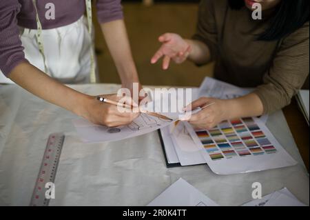 Deux stylistes ou couturiers professionnels discutent et vérifient ensemble de nouvelles esquisses de modèles dans le studio. image rognée Banque D'Images