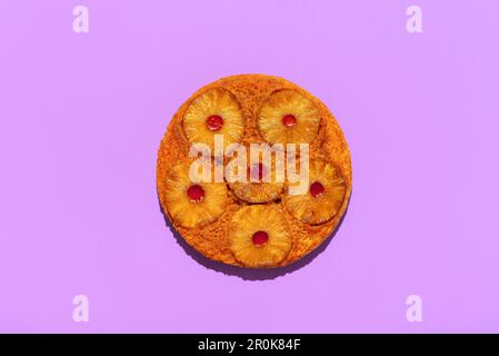 Vue ci-dessus avec un gâteau à l'ananas maison, minimaliste sur une table de couleur pourpre. Gâteau à l'envers avec tranches d'ananas et confiture de fraises. Banque D'Images