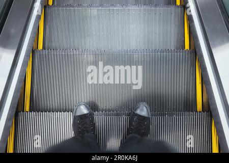 Vue de dessus des jambes des baskets debout sur le marchepied de l'escalator Banque D'Images