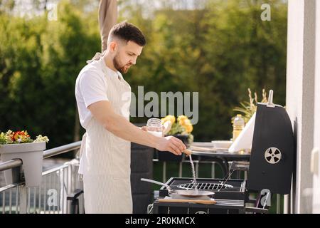 L'homme barbu ajoute du sel sur une casserole en acier au carbone pour assaisonner. Première utilisation d'une poêle classique de France Banque D'Images