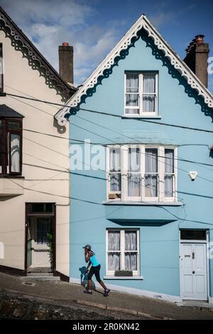 Femme vêtue de bleu en face de la maison bleue Deck of Cards (maisons colorées et escarpées à West View Street), Cobh, Comté de Cork, Irlande, Europe Banque D'Images