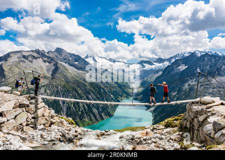 Randonneur sur un pont suspendu au-dessus de la cabane de montagne Olpererhütte en face du panorama des Alpes de Zillertal avec le réservoir Schlegeisspeicher, Banque D'Images