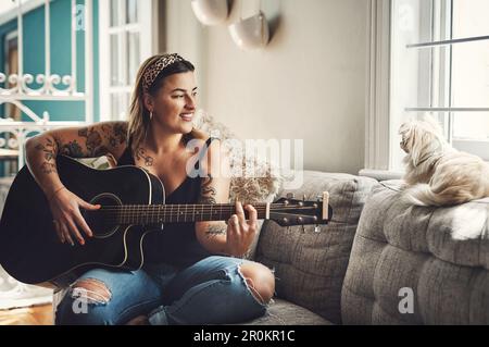 Chaque artiste apprécie un public attentif. une jeune femme jouant de la guitare lors d'une journée de détente à la maison. Banque D'Images