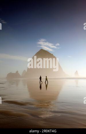 États-Unis, Oregon, Pacific City, les individus marchent le long de Pacific City Beach avec Haystack Rock au loin Banque D'Images