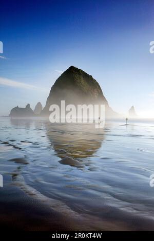 États-Unis, Oregon, Pacific City, les individus marchent le long de Pacific City Beach avec Haystack Rock au loin Banque D'Images