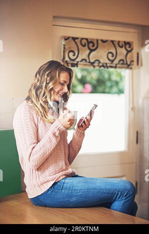 Le temps du café est le temps de rattrapage des médias sociaux. une jeune femme détendue prenant un café et utilisant une tablette numérique à la maison. Banque D'Images