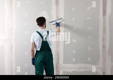 Ouvrier dans un mur uniforme de plâtrage avec couteau à mastiquer à l'intérieur, vue arrière. Espace pour le texte Banque D'Images