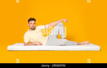 Homme allongé sur un matelas souple sur fond orange Banque D'Images