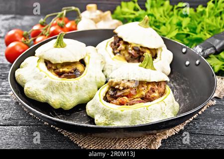 Courge farcie avec du foie, des oignons, des champignons, des tomates et du fromage dans une poêle sur une serviette en toile de fond en bois noir Banque D'Images