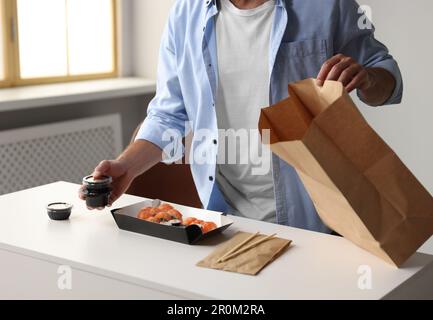 Homme déballant sa commande du restaurant sushi à table dans la salle, fermé Banque D'Images