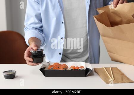 Homme déballant sa commande du restaurant sushi à table dans la salle, fermé Banque D'Images