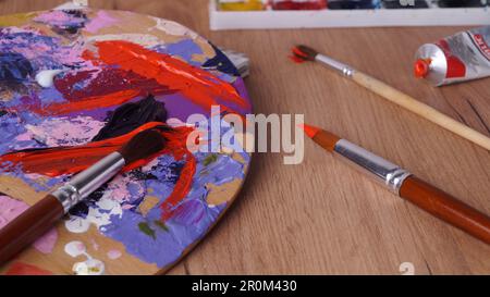 Palette de l'artiste avec des peintures et des pinceaux mélangés sur une table en bois Banque D'Images