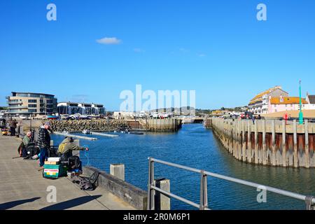 Des hommes pêchant depuis la jetée du port avec des bâtiments de ville à l'arrière, West Bay, Dorset, Royaume-Uni, Europe. Banque D'Images