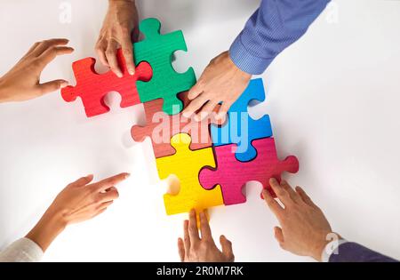 Un groupe de trois jeunes place des puzzles colorés sur la table et présente le concept de coopération, de travail d'équipe, de soutien et d'assistance au bureau. Banque D'Images