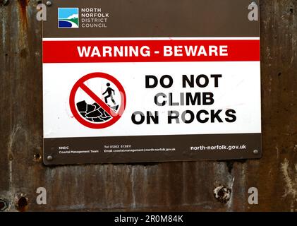 Un panneau d'avertissement sur la promenade pour ne pas monter sur les rochers de défense de la mer à des fins de sécurité sur la côte nord de Norfolk à Sheringham, Norfolk, Angleterre, Royaume-Uni. Banque D'Images