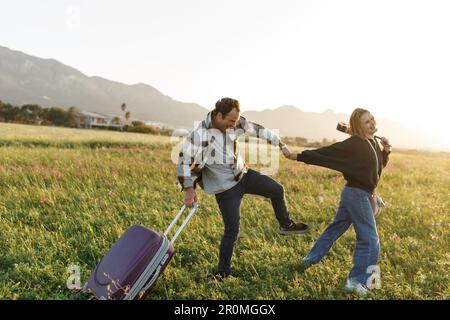 Un jeune couple épris inspiré regarde le plan de vie à l'avenir. Ils sont debout avec une valise et ukulele, tenant les mains. Recherche d'une nouvelle homela Banque D'Images