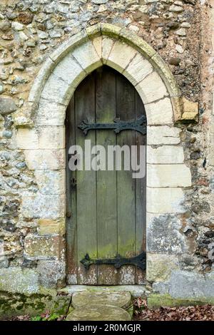 Petite porte étroite en bois voûté avec charnières en métal moulé ornées avec des encadrements en pierre dans le mur de flange de la fierté l'église Saint-Pierre Weston, Suffolk Banque D'Images