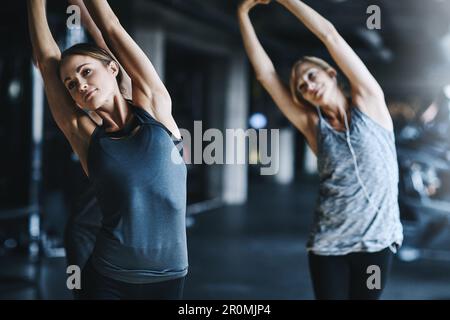 Atteindre leurs objectifs. deux jeunes femmes attirantes s'étirant avant leur entraînement dans la salle de gym. Banque D'Images