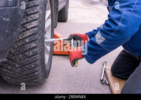 le mécanicien installe et venne la roue sur la voiture à l'aide d'une clé à cliquet Banque D'Images