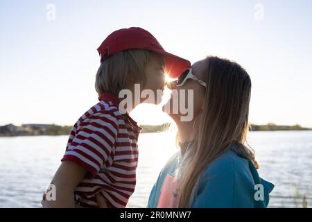 gros plan de la mère et du fils face à face en contre-jour du soleil couchant sur le lac. plaisir du moment, sentiments tendres, passe-temps agréable. Position Banque D'Images