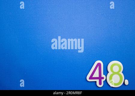 Le numéro 48, placé sur le bord d'un fond bleu, photographié par le dessus, de couleur violet et vert. Banque D'Images