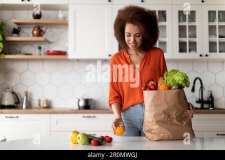 Happy Young Black Lady Déballage du sac en papier avec des provisions après les achats de nourriture Banque D'Images