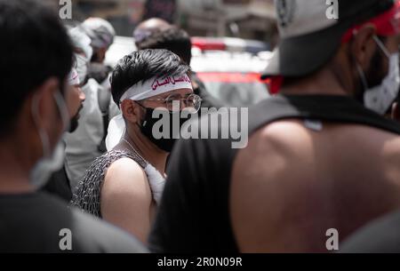 Un groupe de personnes portant des masques protecteurs se promenant dans une rue de la ville pendant la journée, Muharram Banque D'Images
