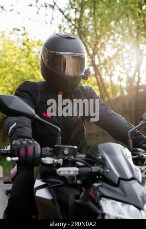 Motard non reconnaissable dans un casque de protection et une veste en cuir confortable avec gants de main à bord d'une moto par beau temps en campagne Banque D'Images